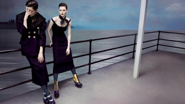 Zwei Frauen in eleganter Kleidung posieren auf einem Pier am Meer.