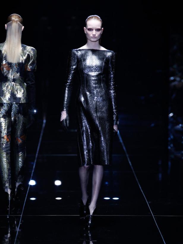 Eine Frau in einem glänzenden, schlangenlederartigen Kleid auf dem Laufsteg.