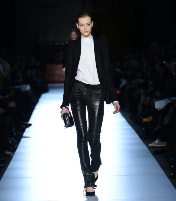 Eine Frau in Lederhose und Blazer läuft auf dem Laufsteg.