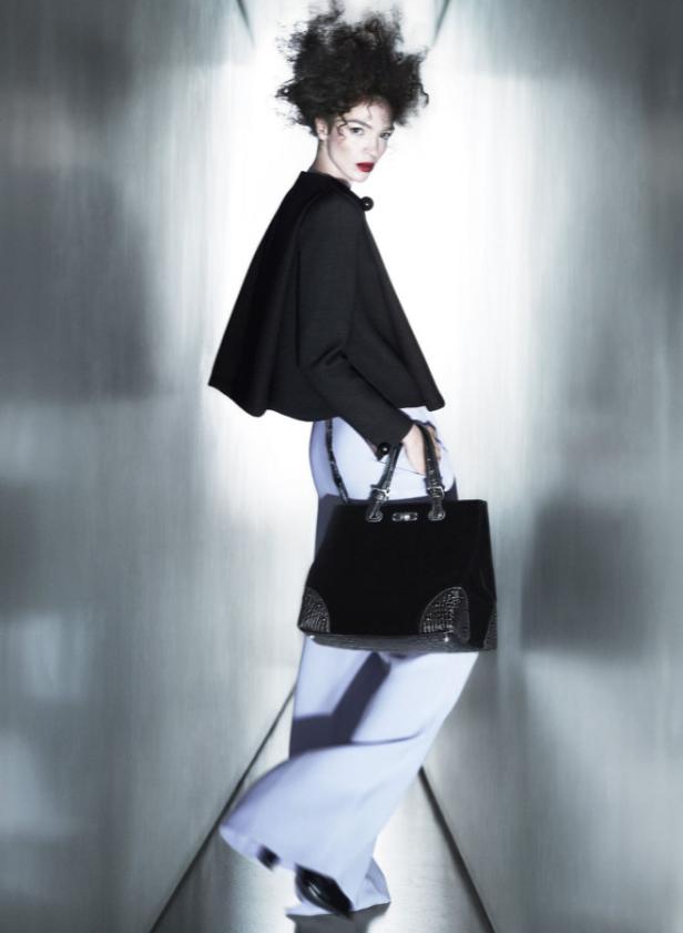 Eine Frau mit Afro-Frisur, Cape und Handtasche posiert in einem futuristischen Gang.