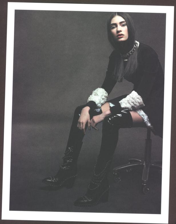 Eine Frau sitzt auf einem Stuhl und trägt ein schwarzes Kleid und Stiefel mit Ketten.