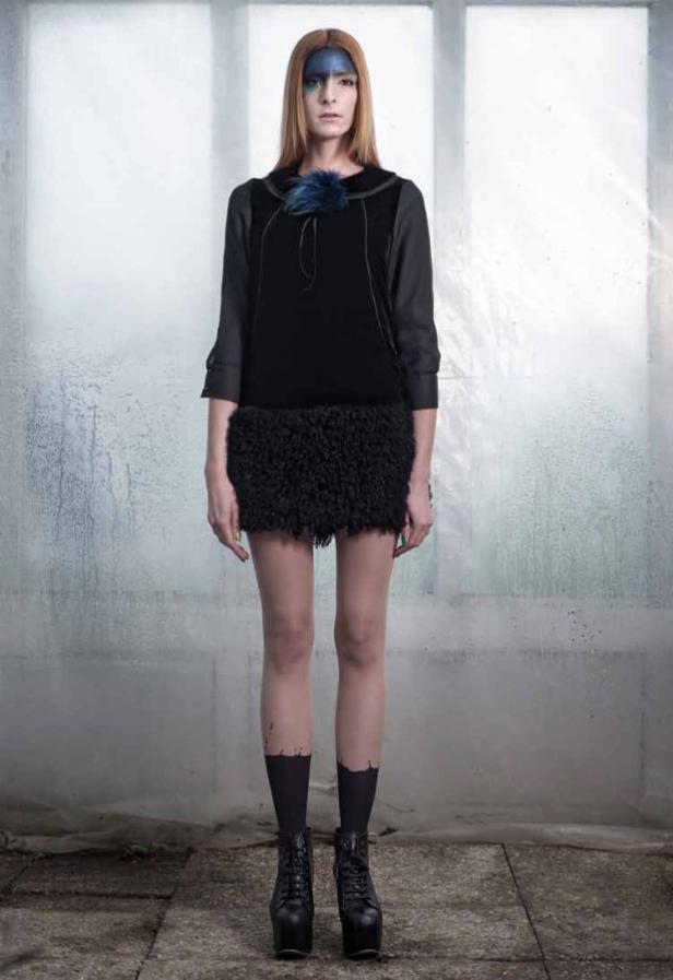 Eine Frau mit blauer Farbe im Gesicht trägt ein schwarzes Kleid und Stiefel mit hohen Absätzen.