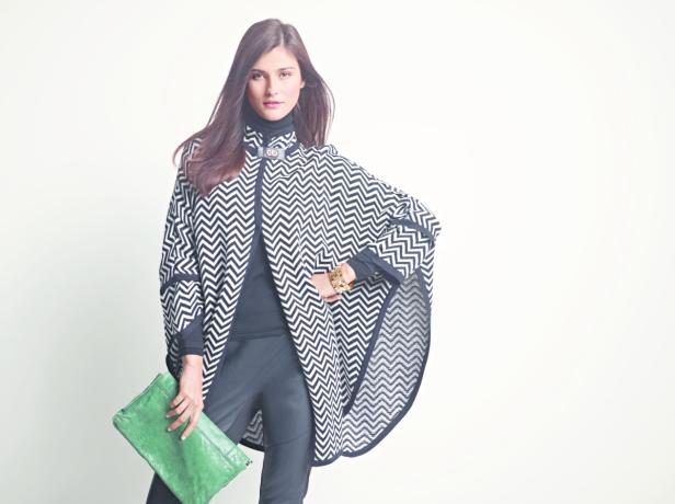 Eine Frau posiert mit einem Zickzack-Poncho und einer grünen Clutch vor einem weißen Hintergrund.