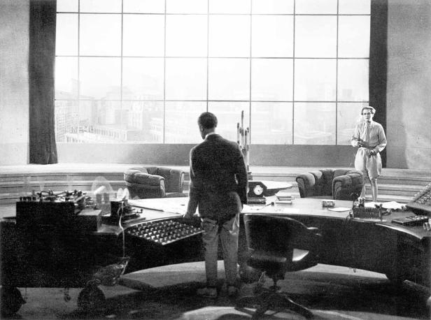 Ein Mann steht in einem Büro mit einem großen Fenster und blickt auf die Stadt.