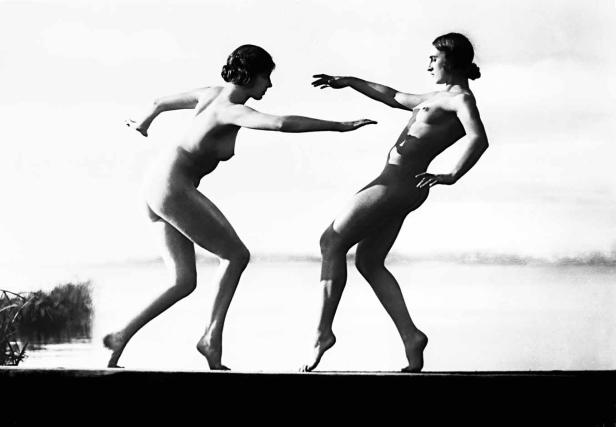 Zwei nackte Frauen posieren an einem Seeufer.