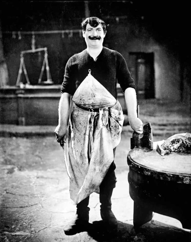 Ein Metzger mit Schnurrbart steht in einer Metzgerei.