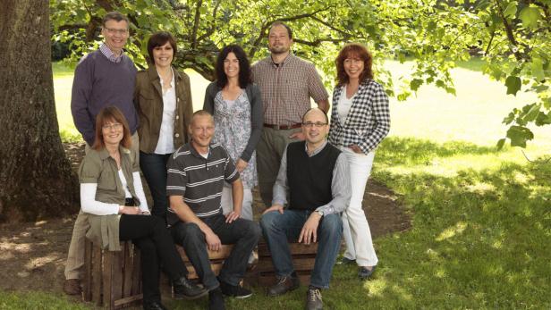 Eine Gruppe von acht Personen posiert im Freien für ein Foto.