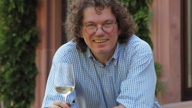 Ein lächelnder Mann mit Brille hält ein Glas Weißwein.