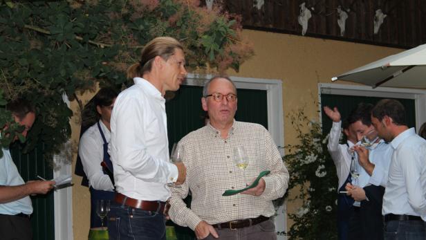 Zwei Männer unterhalten sich bei einer Weinprobe im Freien.