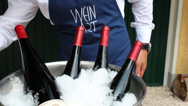 Ein Kellner mit einer Schürze mit der Aufschrift „Wein Art“ präsentiert Weinflaschen in Eis.
