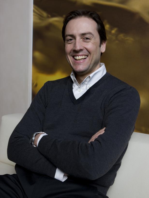 Ein lächelnder Mann sitzt mit verschränkten Armen auf einem Sofa.