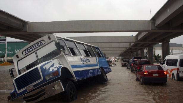 Ein Bus der Marke „Costera“ steht schräg im Hochwasser unter einer Brücke.