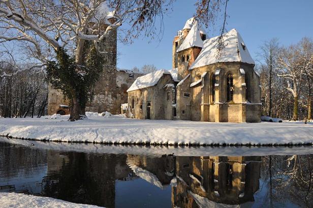 Ein schneebedecktes Schloss wird im ruhigen Wasser eines Burggrabens reflektiert.