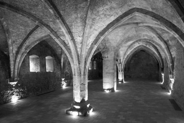 Ein Gewölbekeller mit Steinpfeilern und schwachem Licht.
