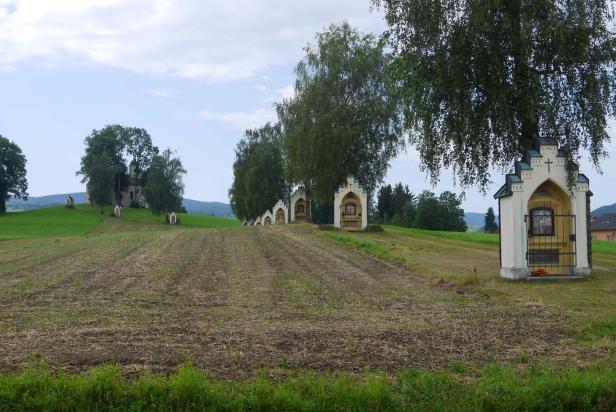 Eine Reihe von Bildstöcken führt zu einer Kirche auf einem Hügel.