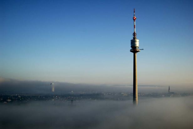 Der Donauturm ragt über eine nebelverhangene Stadtlandschaft hinaus.