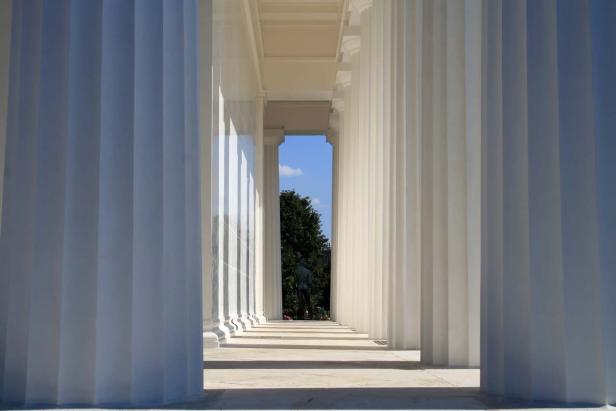 Blick durch eine Kolonnade auf eine Statue im Freien.