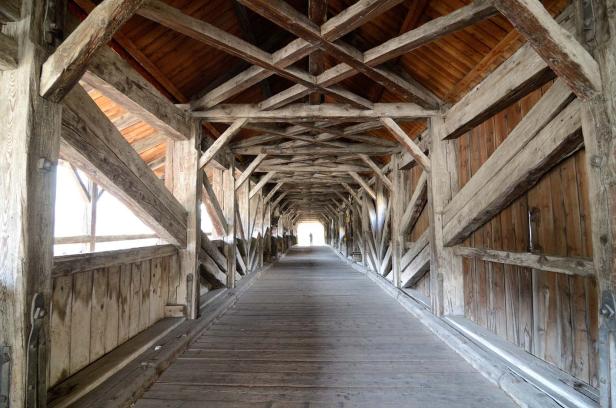 Blick in das Innere einer alten, hölzernen Brücke mit einer Person am Ende.