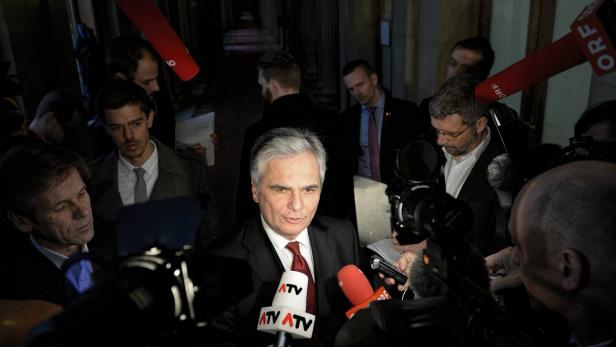 Ein Mann im Anzug wird von Mikrofonen und Kameras umringt.