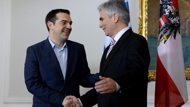 Alexis Tsipras schüttelt einem Mann die Hand, im Hintergrund Flaggen von Griechenland und Österreich.