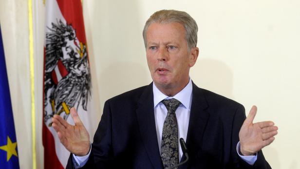 Ein Mann in Anzug gestikuliert vor der österreichischen und der EU-Flagge.