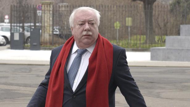 Ein Mann mit Anzug und rotem Schal steht im Freien.