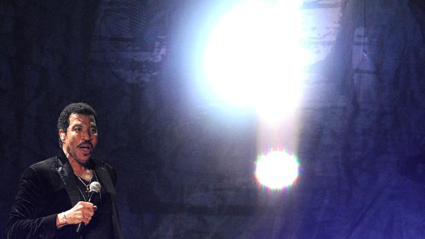 Lionel Richie singt auf einer Bühne in ein Mikrofon.