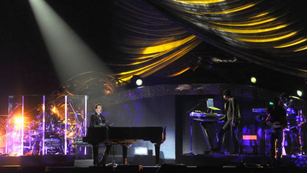 Lionel Richie spielt Klavier auf einer Bühne mit Schlagzeugern und anderen Musikern.