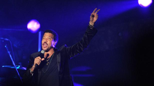 Lionel Richie singt mit erhobener Hand auf einer Bühne.