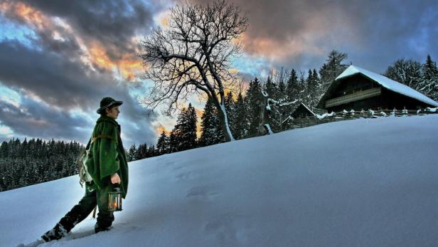 Ein Junge mit Laterne wandert im Winter durch eine verschneite Landschaft.