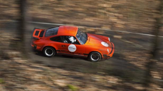 Ein orangefarbener Porsche 911 fährt auf einer Landstraße.