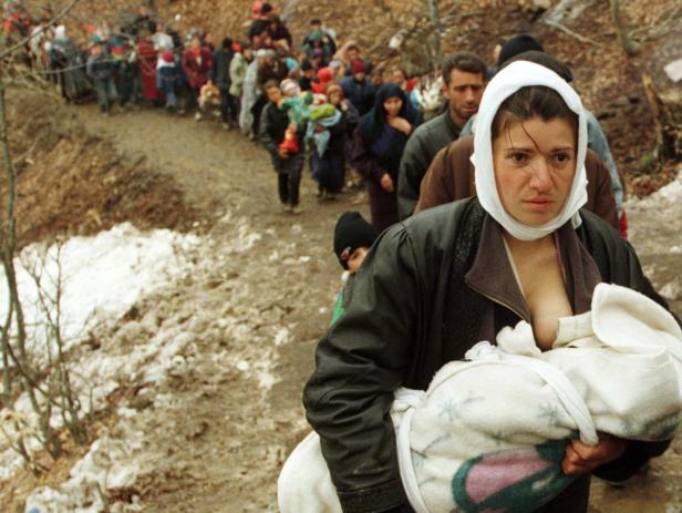 Eine Frau mit Kopftuch trägt ein Baby inmitten einer Gruppe von Flüchtlingen.