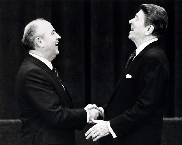 Ronald Reagan und Michail Gorbatschow schütteln sich die Hände und lachen.