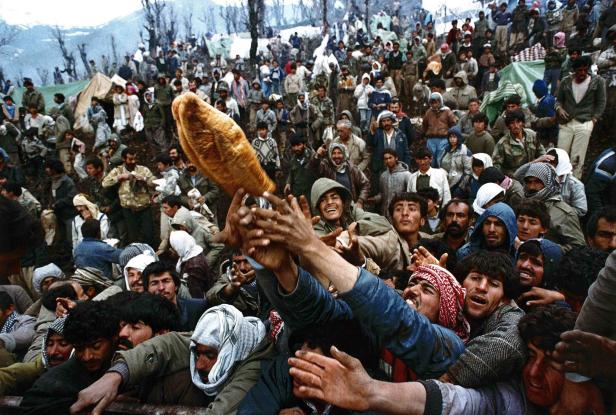 Eine Menschenmenge drängt sich um ein großes Brot, das in die Höhe gehalten wird.