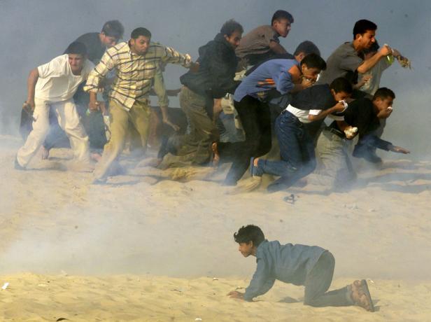 Eine Gruppe von Menschen rennt auf einem Sandstrand vor Tränengas davon.