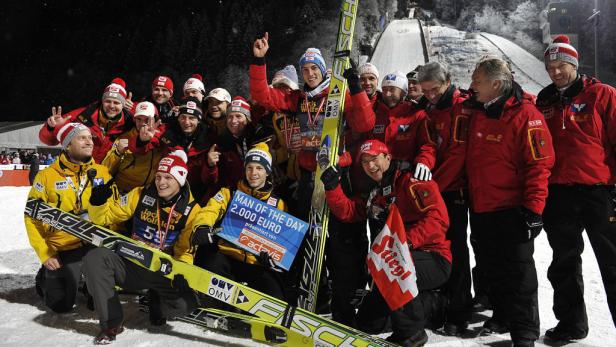 Eine Gruppe Skispringer und Trainer feiert einen Sieg mit einem Preisgeld-Scheck.