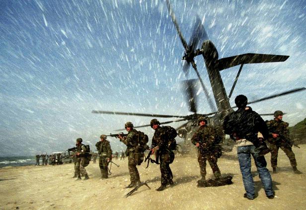 Soldaten stehen im Schneetreiben vor einem Hubschrauber am Strand.