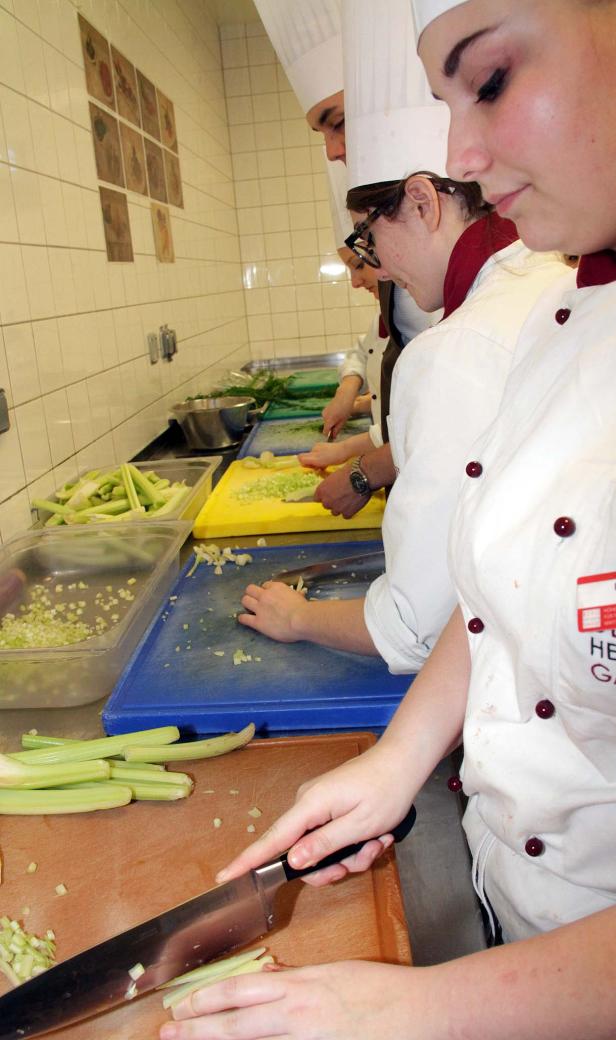 Mehrere Köche in Kochuniformen schneiden Gemüse in einer Küche.