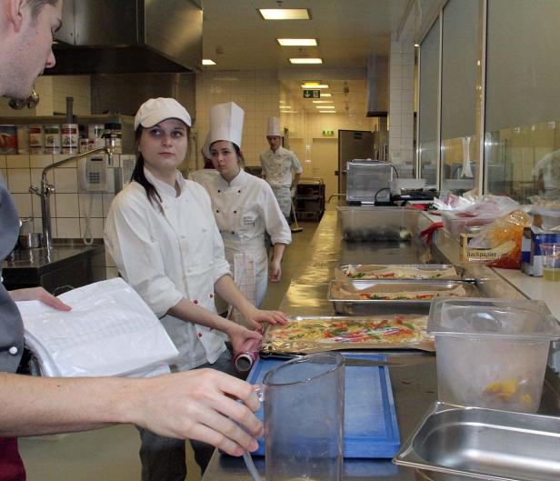 Mehrere Köche bereiten in einer Großküche Speisen zu.