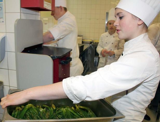 Eine junge Köchin bereitet in einer Küche grüne Bohnen zu.