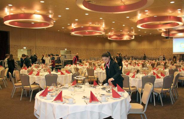 Ein großer Saal mit runden Tischen, die für eine Veranstaltung gedeckt sind.