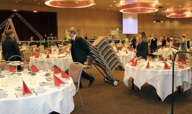 Ein Mann transportiert Stühle in einem Saal mit gedeckten Tischen.