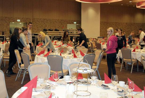 Mehrere Personen bereiten Tische für eine Veranstaltung vor.