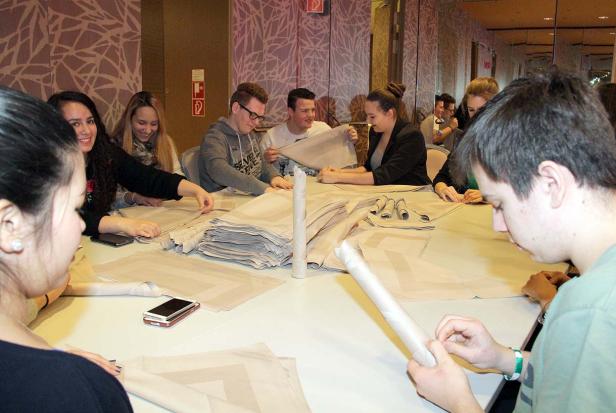 Eine Gruppe von Menschen faltet Stoffservietten an einem Tisch.