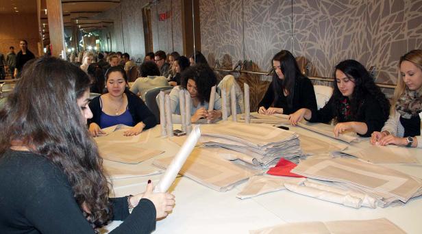 Eine Gruppe von Frauen sitzt an einem Tisch und verpackt Servietten und Besteck.