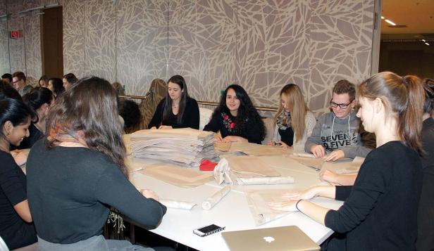 Mehrere Personen sitzen an einem Tisch und verpacken Gegenstände in Papier.