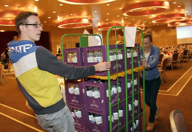 Zwei Personen schieben einen Wagen mit Vöslauer-Wasserflaschen in einem Saal.