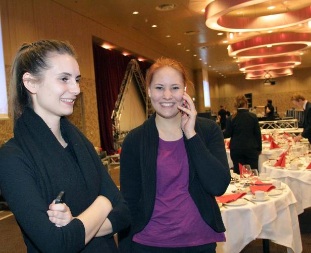 Zwei Frauen stehen in einem Veranstaltungsraum, eine telefoniert.