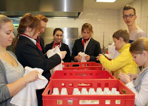 Mehrere Personen putzen Gläser in roten Kisten in einer Küche.