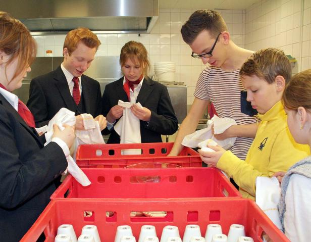 Eine Gruppe von Jugendlichen trocknet Geschirr in einer Küche ab.